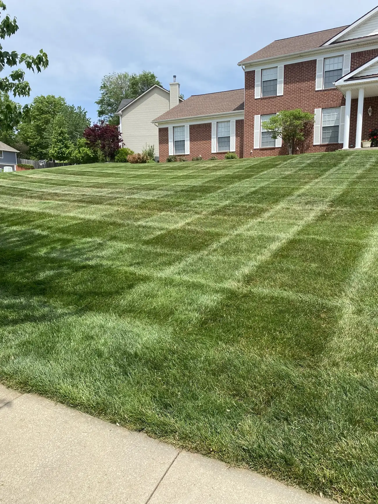 A front lawn mowed in a crisp diamond checkerboard pattern before a brick two-story home in the Northland